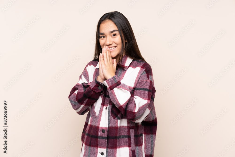 Young Indian woman isolated on beige background keeps palm together. Person asks for something Young Indian woman isolated on beige background keeps palm together. Person asks for something