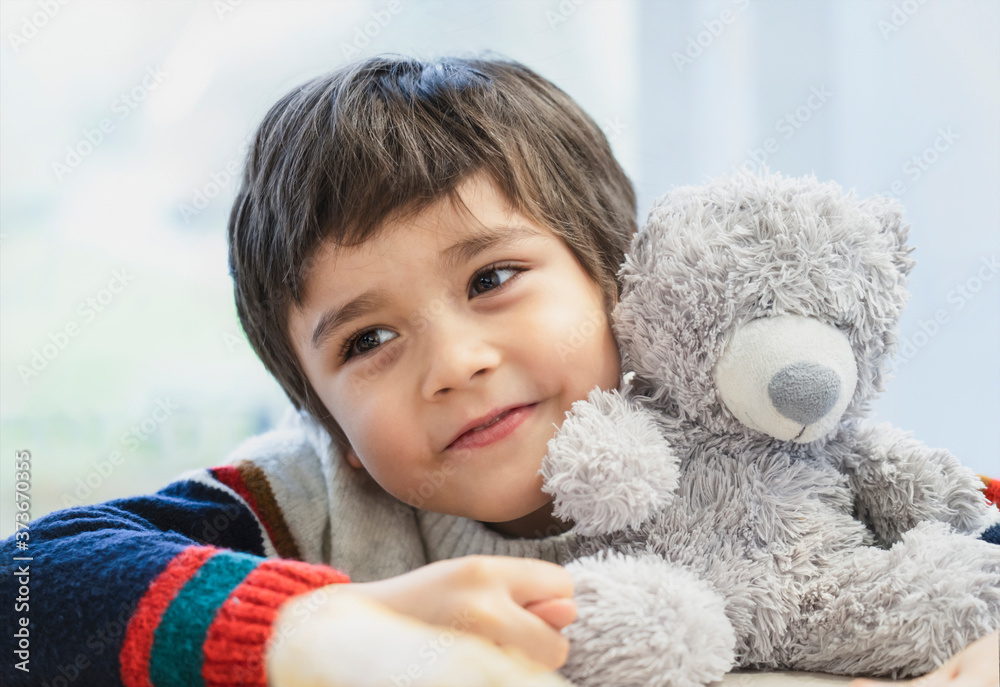 Φωτογραφία High key light portrait cute boy laying his head on teddy bear and looking out with beautiful brown eyes, Adorable Child playing with toys and relaxing while waiting for food in cafe