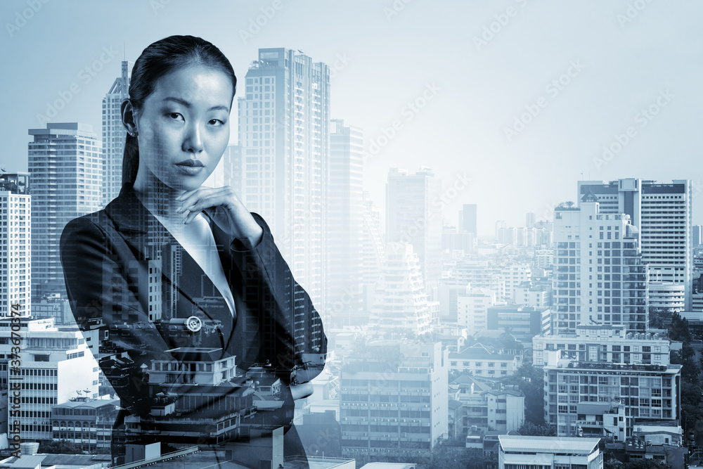 Attractive young Asian business woman in suit with hand on chin thinking how to succeed, new career opportunities, MBA. Bangkok on background. Double exposure. Attractive young Asian business woman in suit with hand on chin thinking how to succeed, new career opportunities, MBA. Bangkok on background. Double exposure.