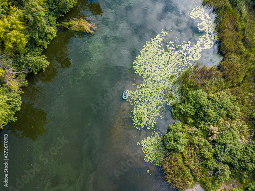 Aerial drone view. Fishing boat on green water near the shore. Algae bloom in the river, green pattern on the water.