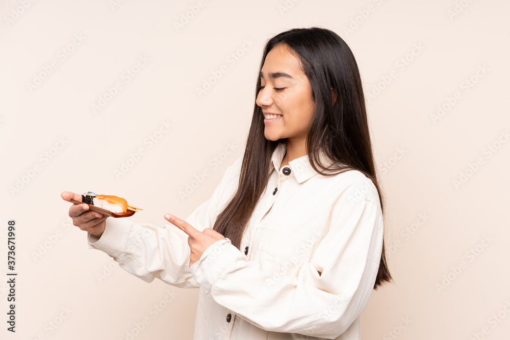 Young Indian woman holding sushi isolated on beige background and pointing it Young Indian woman holding sushi isolated on beige background and pointing it