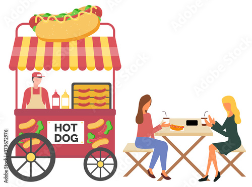 Vendor male standing with hotdog cart, fastfood retail. Women eating sausage and drinking coffee, urban marketplace with wheels, lunch outdoor vector