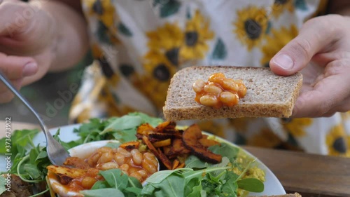 Female putting beans on a slice of brown bread with a fork. Full English breakfast consist of scramble, mushrooms and vegetables. Healthy lifestyle concept