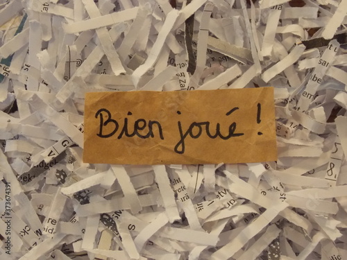 Well done handwritten in French on brown paper amid paper shreds 