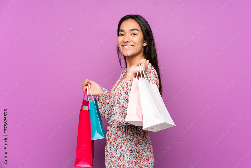 Young Indian woman isolated on purple background holding shopping bags and smiling Young Indian woman isolated on purple background holding shopping bags and smiling