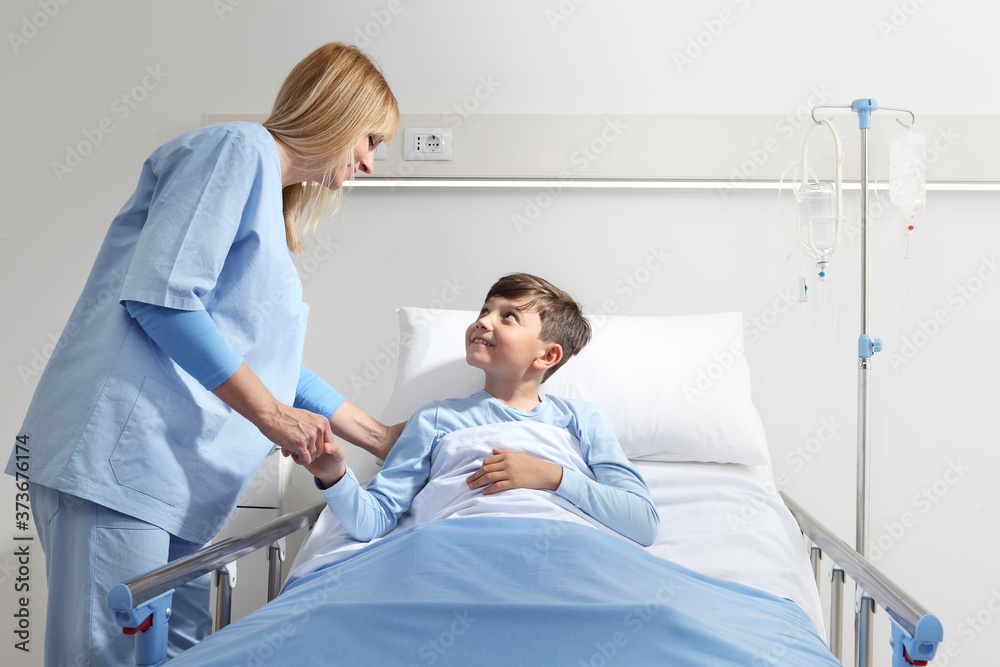 Little boy lying in hospital bed holding hands with smiling nurse . Little boy lying in hospital bed holding hands with smiling nurse .