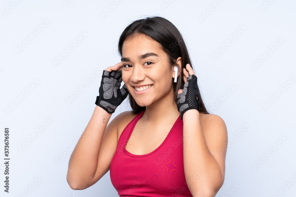 Young Indian sport woman isolated on blue background listening music Young Indian sport woman isolated on blue background listening music