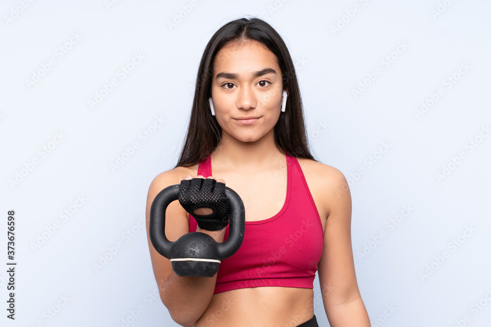 Young Indian sport woman isolated on blue background making weightlifting with kettlebell and looking to the front Young Indian sport woman isolated on blue background making weightlifting with kettlebell and looking to the front