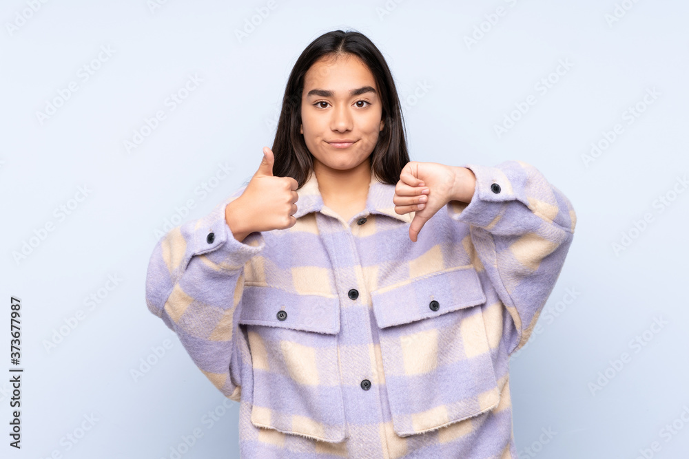 Young Indian woman isolated on blue background making good-bad sign. Undecided between yes or not Young Indian woman isolated on blue background making good-bad sign. Undecided between yes or not