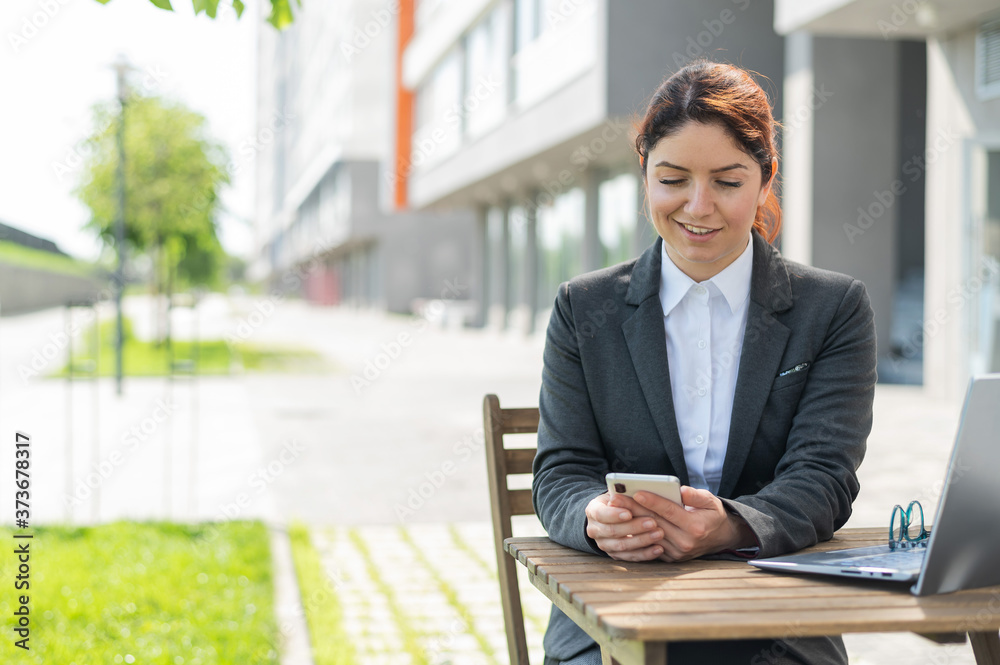 Smilling caucasian woman sits at a wooden table on a summer terrace and uses a smartphone Smilling caucasian woman sits at a wooden table on a summer terrace and uses a smartphone