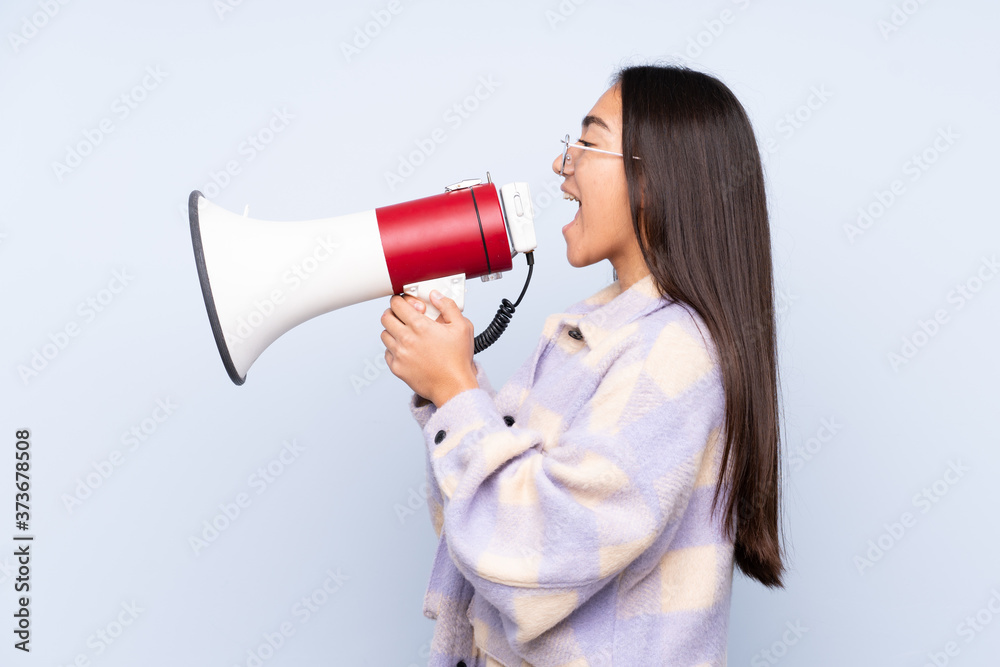 Young Indian woman isolated on blue background shouting through a megaphone Young Indian woman isolated on blue background shouting through a megaphone
