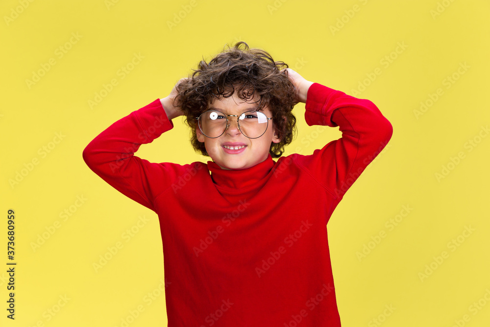 Shocked. Portrait of pretty young curly boy in red wear on yellow studio background. Childhood, expression, education, fun concept. Preschooler with bright facial expression and sincere emotions. Shocked. Portrait of pretty young curly boy in red wear on yellow studio background. Childhood, expression, education, fun concept. Preschooler with bright facial expression and sincere emotions.