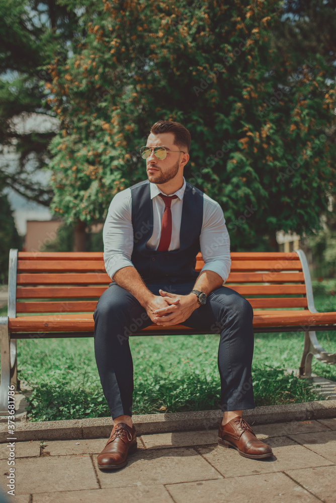 Fototapeta premium a young sexy businessman in a suit sitting in park on job break