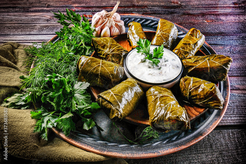 Traditional Georgian and Greek dolma in grape leaves on a wooden table with sour cream sauce and herbs.