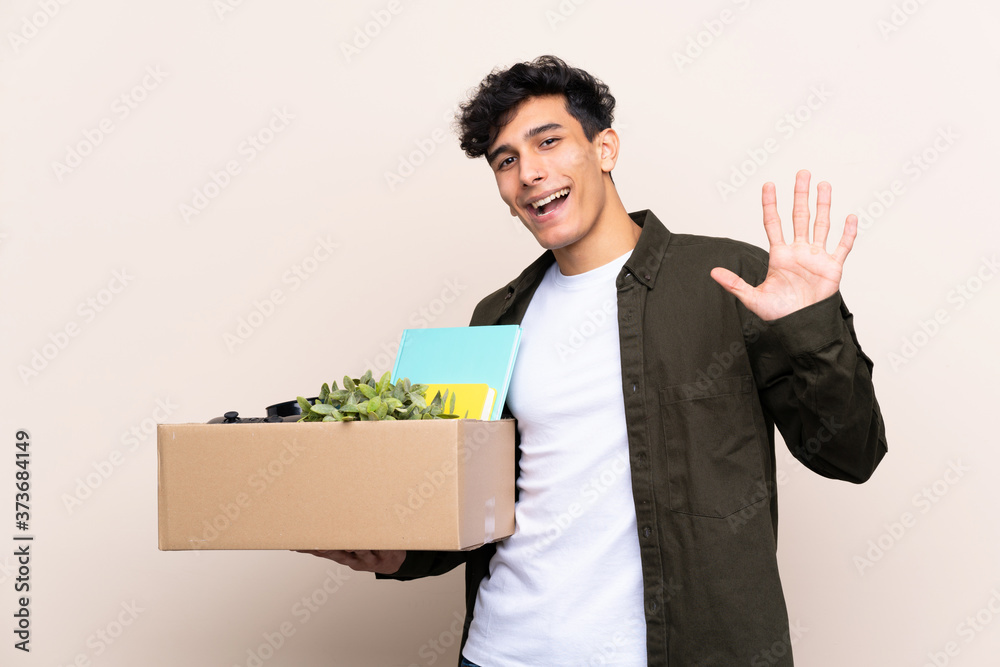 Young Argentinian man moving in new home over isolated background saluting with hand with happy expression Young Argentinian man moving in new home over isolated background saluting with hand with happy expression