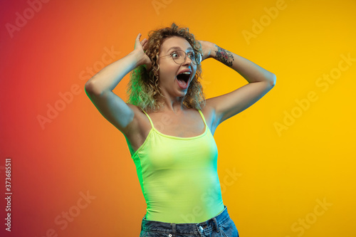 Crazy shocked. Caucasian young woman's portrait isolated on gradient studio background in neon. Beautiful female curly model in casual style. Concept of human emotions, facial expression, youth, sales