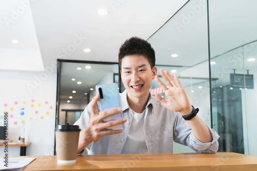 Young smart asian business man in casual shirt at the office,Greeting colleagues through video conferencing.
