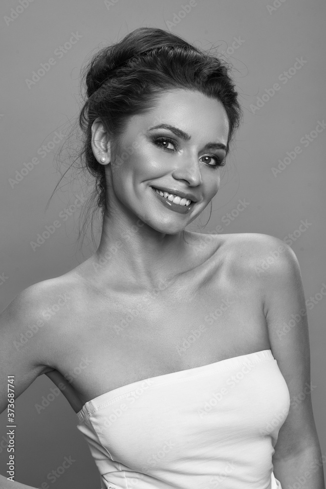 Young beautiful caucasian woman face. Girl with perfect skin, natural make-up and brunette hair in sloppy high bun looking at you. Fashion studio portrait against azure background. Wellness concept Young beautiful caucasian woman face. Girl with perfect skin, natural make-up and brunette hair in sloppy high bun looking at you. Fashion studio portrait against azure background. Wellness concept