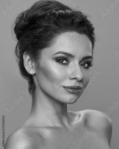 Young beautiful caucasian woman face. Girl with perfect skin, natural make-up and brunette hair in sloppy high bun looking at you. Fashion studio portrait against azure background. Wellness concept