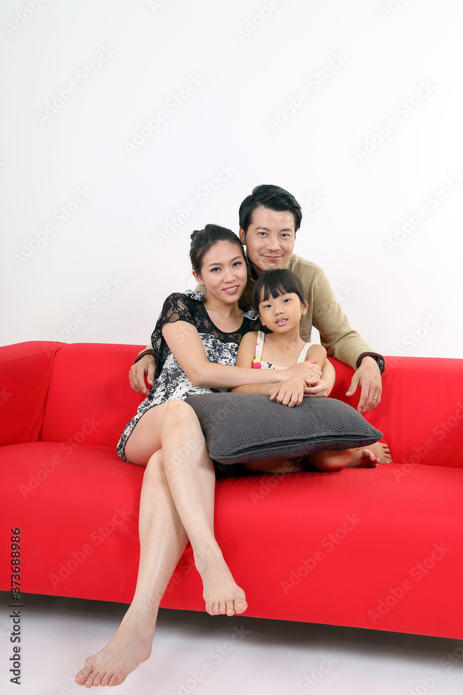 South East Asian young couple father mother daughter parent girl child on red sofa look at camera on white background