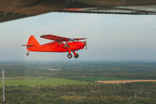 Vintage red small plane Stinson in flight over the green forest.