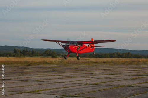 A vintage red Stinson small plane flies low over a private concrete runway.