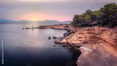 Boats moored beside stone jetty at sunset, overlooked by beautiful rocks and trees, with calm sea, Betlem, Mallorca, Spain.