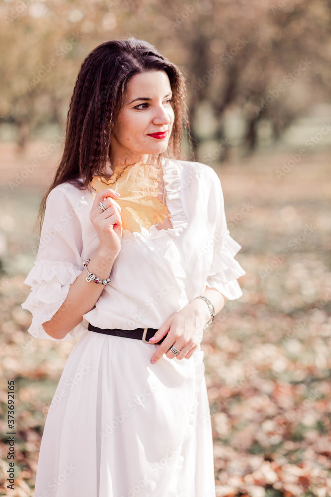 Beautiful brunette girl with long hair in a white dress posing in an autumn park. Beautiful brunette girl with long hair in a white dress posing in an autumn park.