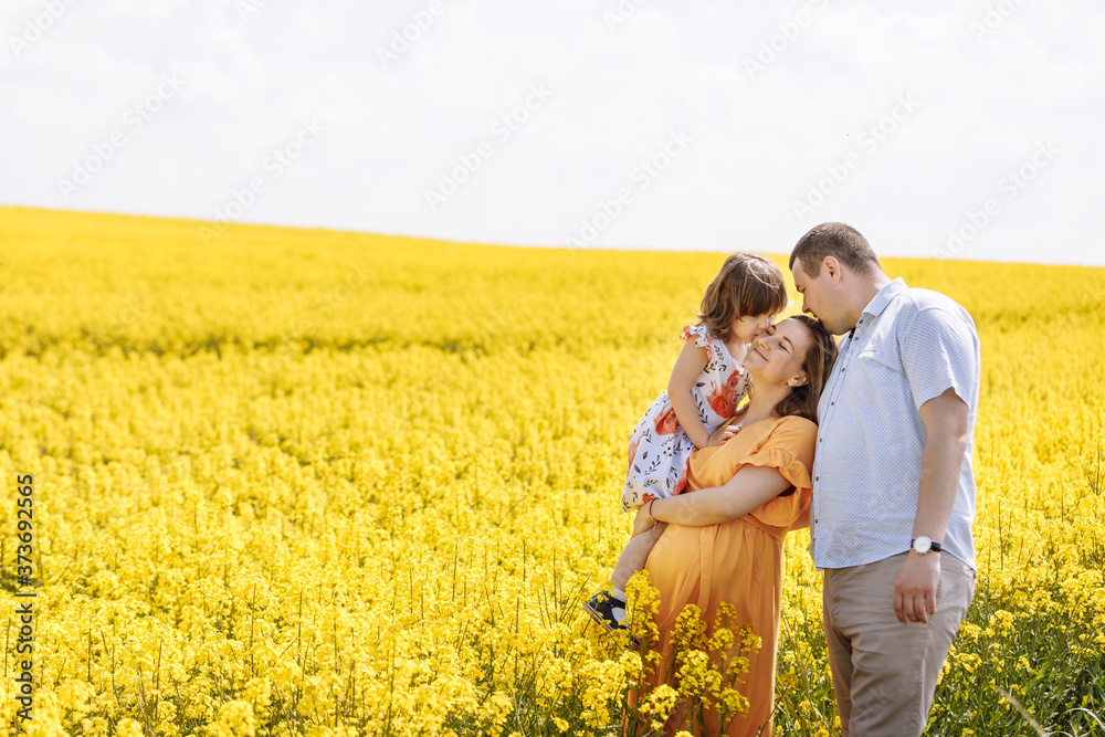 young happy family among the yellow flowering field. Family rest. Pregnant mother, the father and the little daughter have a rest among yellow colza. young happy family among the yellow flowering field. Family rest. Pregnant mother, the father and the little daughter have a rest among yellow colza.