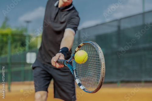 Close Up of Man Playing Tennis At Court And Beating The Ball With a Racket. Player is Hitting Ball With Racket While Playing Match © Akaberka
