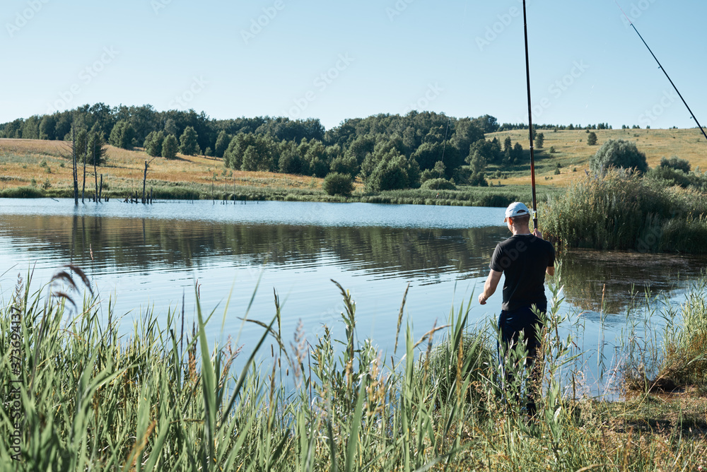 Summer fishing for fishing rod. A fisherman stands against a background of a beautiful, calm lake with reflection of trees. A beautiful scene of outdoor activities