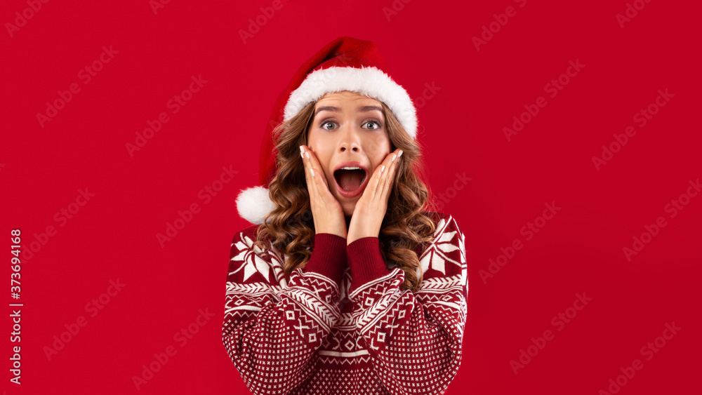 Christmas celebration. Excited young woman in Santa hat and warm winter sweater over red background Christmas celebration. Excited young woman in Santa hat and warm winter sweater over red background