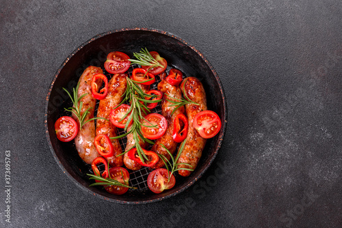 Grilled sausages with vegetables and spices on black background