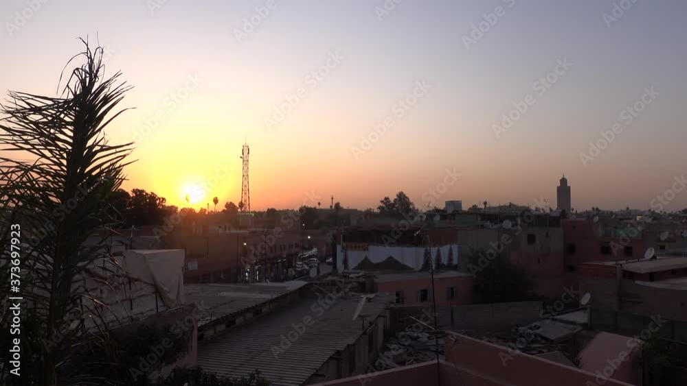 Stunning orange sunset sky over the Marrakech medina city and palm tree leaves moving with wind from viewpoint terrace during travel vacations in Morocco. Stunning orange sunset sky over the Marrakech medina city and palm tree leaves moving with wind from viewpoint terrace during travel vacations in Morocco.