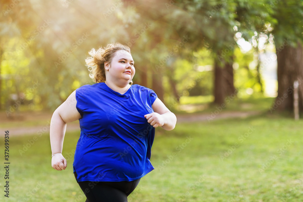 Young plus size blonde is jogging in the park on a summer sunny evening. Healthy lifestyle concept Young plus size blonde is jogging in the park on a summer sunny evening. Healthy lifestyle concept