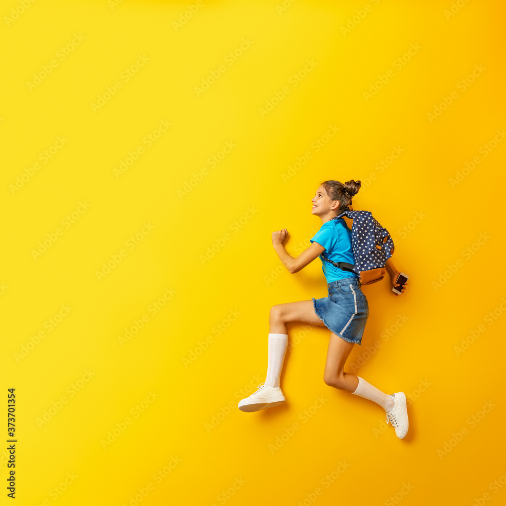 Back to school! Cute hardworking schoolgirl Jogging on a yellow background.