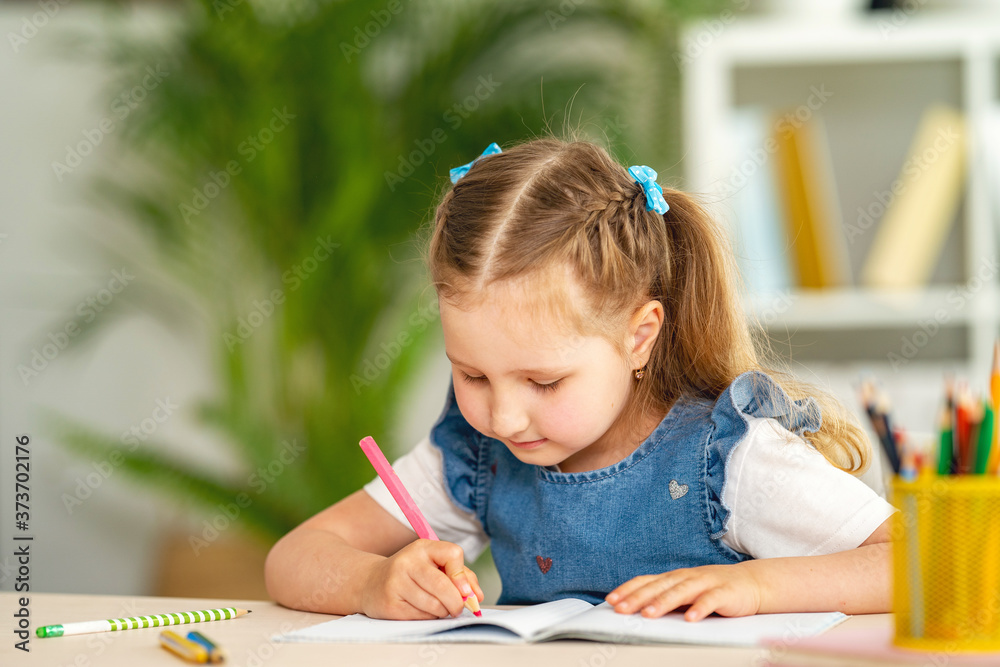 little girl is sitting at a table and writing in a notebook. learning concepts little girl is sitting at a table and writing in a notebook. learning concepts