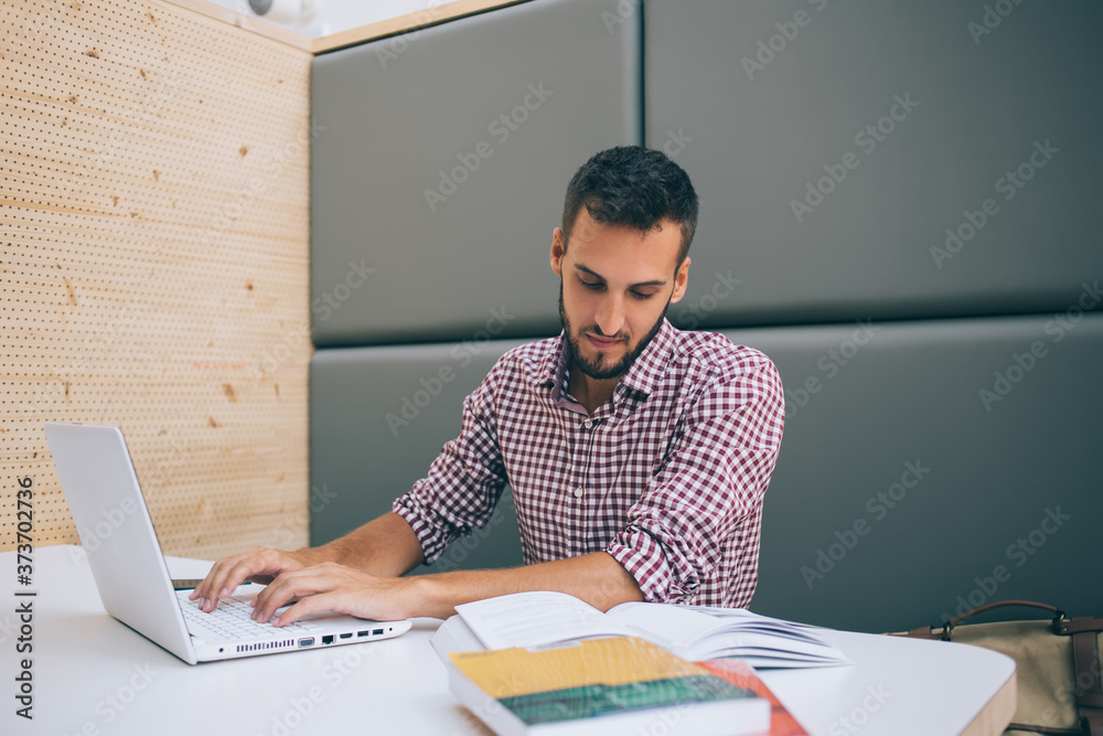Focused man using laptop reading literature at workplace Focused man using laptop reading literature at workplace