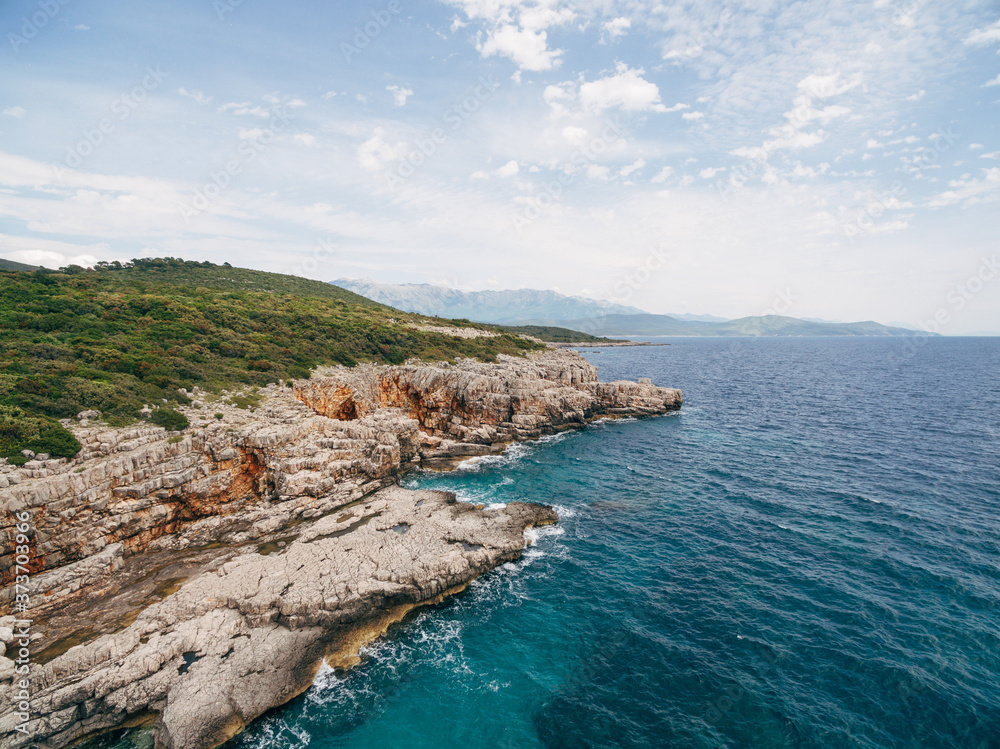 Rocky seaside near Veslo camping in Montenegro. Azure blue water, white waves hitting the rocks, sunny summer day, aerial drone view.