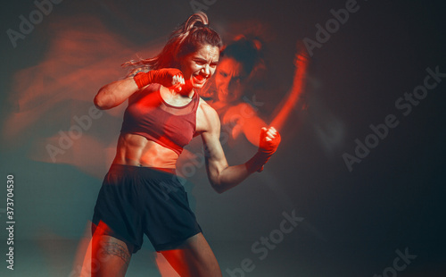 Cool female fighter in boxing bandages trains in studio in red neon light. Mixed martial arts poster. Long exposure shot © Georgii