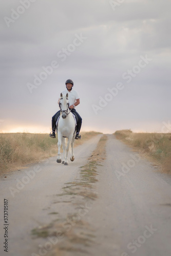 Rider on horseback walking along a path with his white horse. Horse riding in the open air.