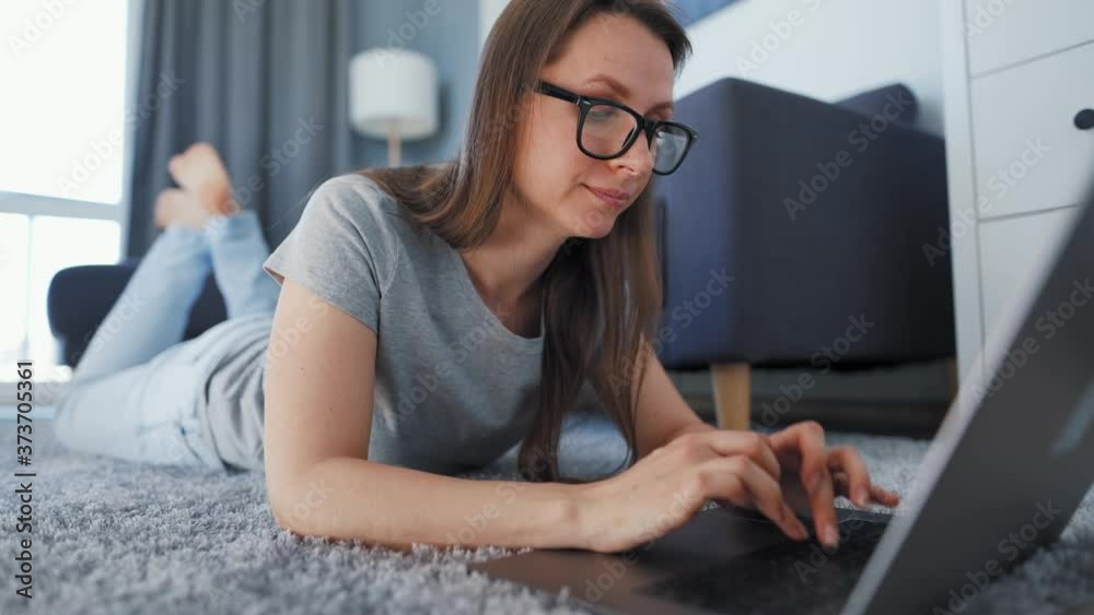 Woman is lying on the floor and working on a laptop. Concept of remote work. Woman is lying on the floor and working on a laptop. Concept of remote work.