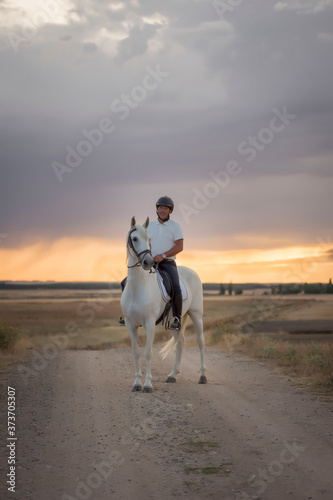 Rider on horseback walking along a path with his white horse. Horse riding in the open air. © fuen30
