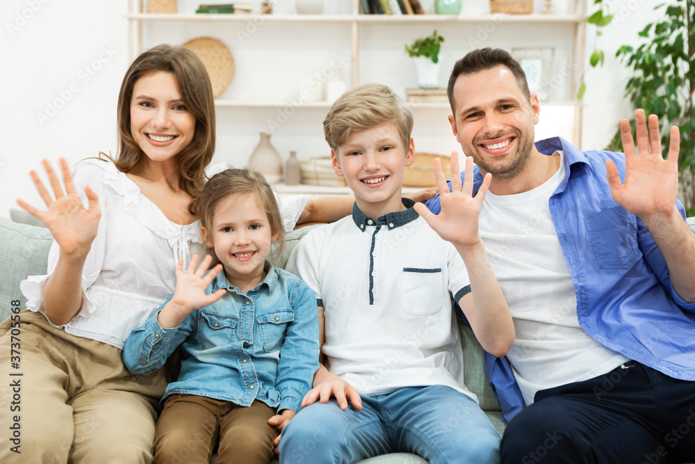 Family Of Four Waving Hello Greeting Sitting On Sofa Indoor Family Of Four Waving Hello Greeting Sitting On Sofa Indoor