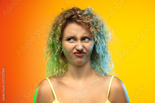 Disguasted. Close up caucasian young woman's portrait on gradient studio background in neon. Beautiful female curly model in casual style. Concept of human emotions, facial expression, youth, sales
