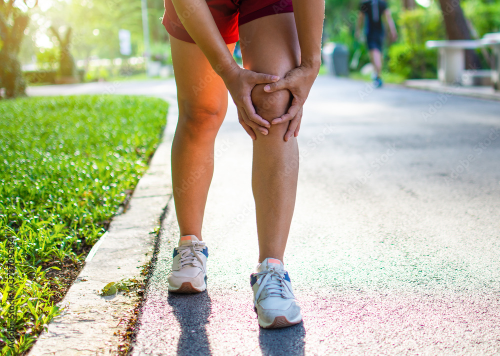 Exercise concept injury: Asian woman grasping her knees while running on park street. Taken in the morning sunlight