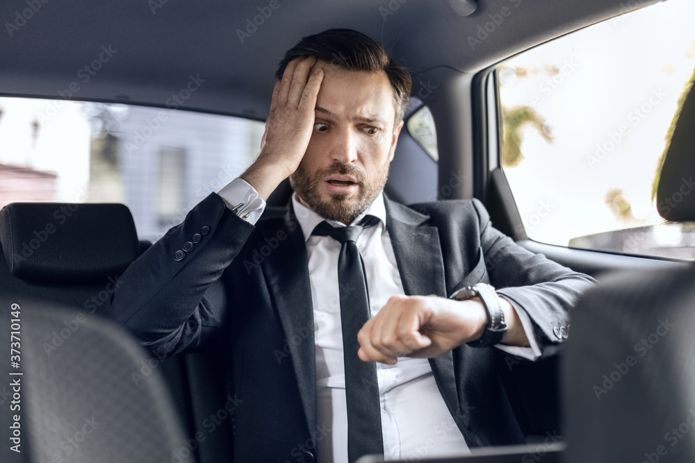 Worried businessman looking at his watch while going by car Worried businessman looking at his watch while going by car