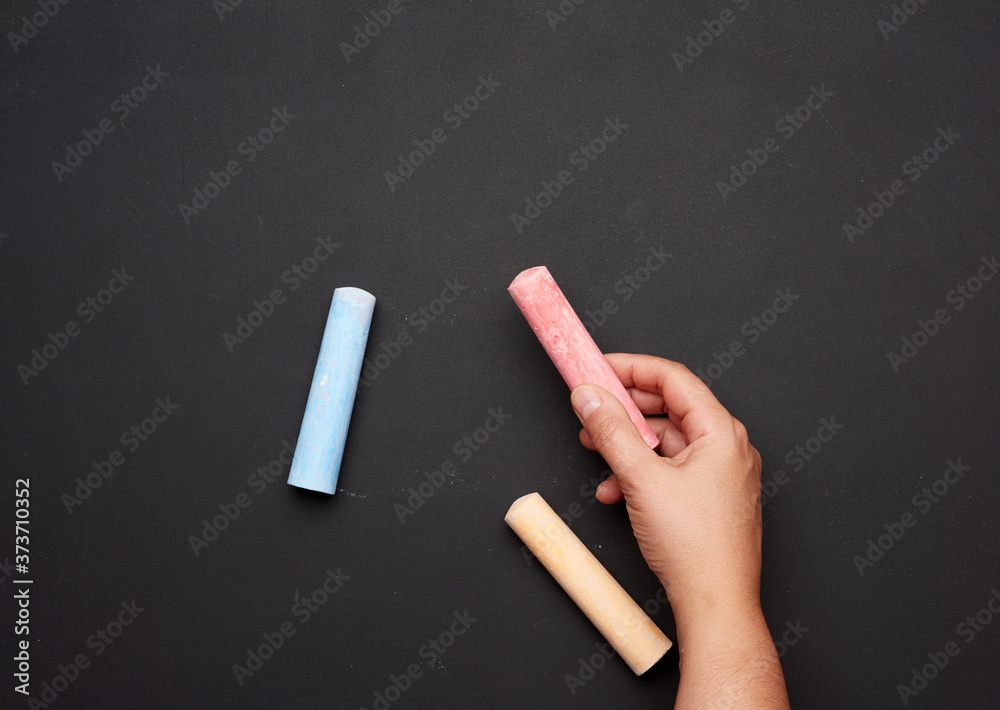 female hand holding red chalk on a background of an empty black chalk board female hand holding red chalk on a background of an empty black chalk board