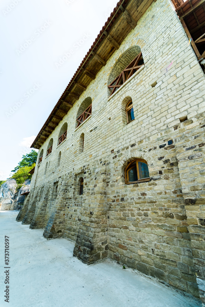 Fototapeta premium Old wall with peeling paint. Scratched stained plaster and closed windows. View from below.