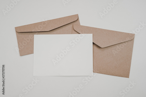 Blank white paper on the two brown paper envelope. Mock-up of horizontal blank greeting card. Top view of Craft paper envelope on white background. Flat lay of stationery. Minimalism style. © Pungu x